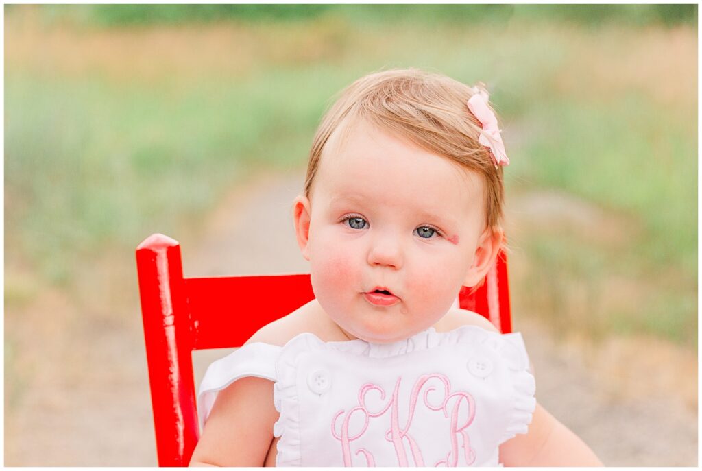 One year old sits in a red chair for Hughes family outdoor session