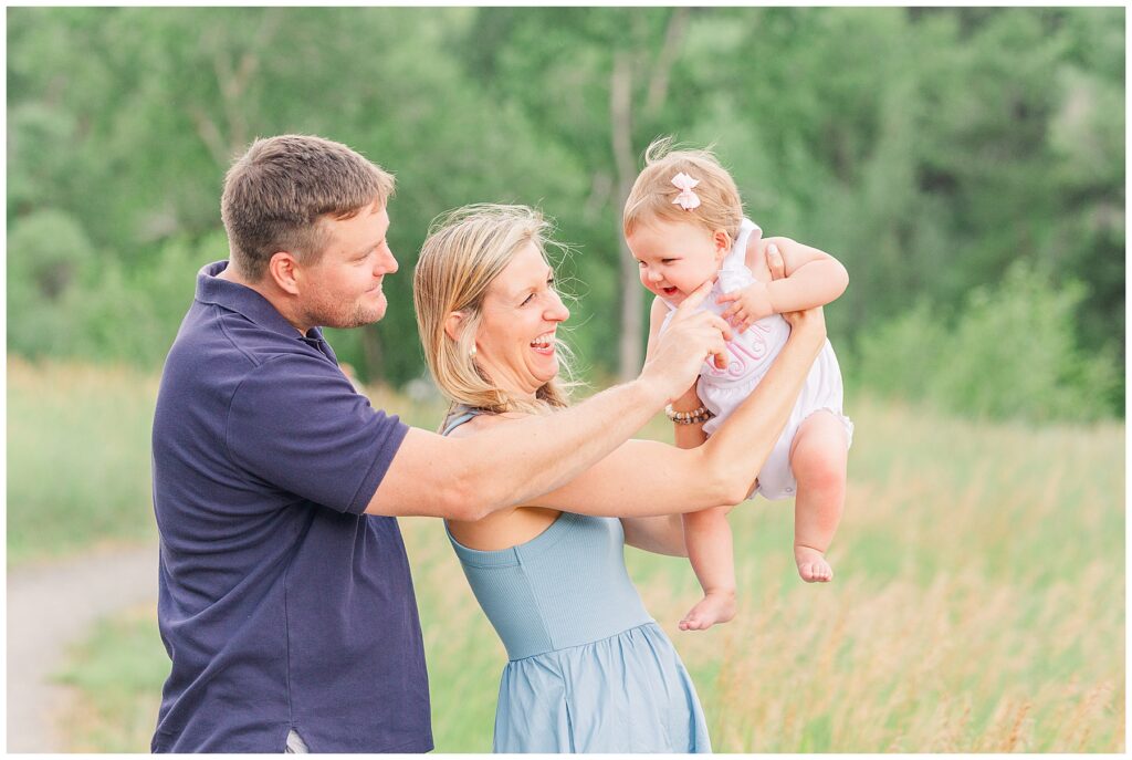 Mom and dad smiles at their baby girl as she is being held up by her mother for Hughes family outdoor session