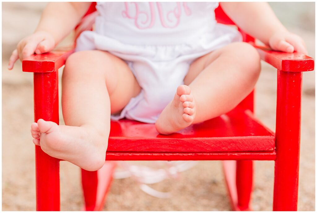 Close up of one-year-old baby girls feet while sitting in a red chair for Hughes family outdoor session