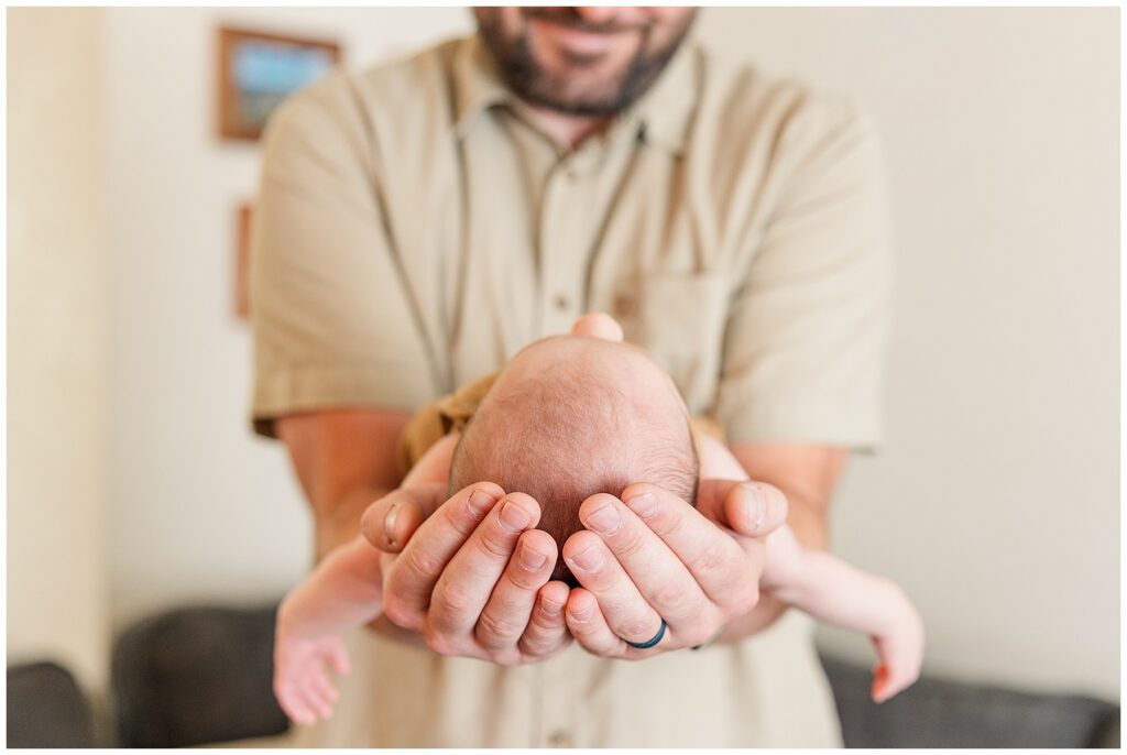 Dad holds his newborn with both hands and looks into his eyes for this in-home Colorado newborn session