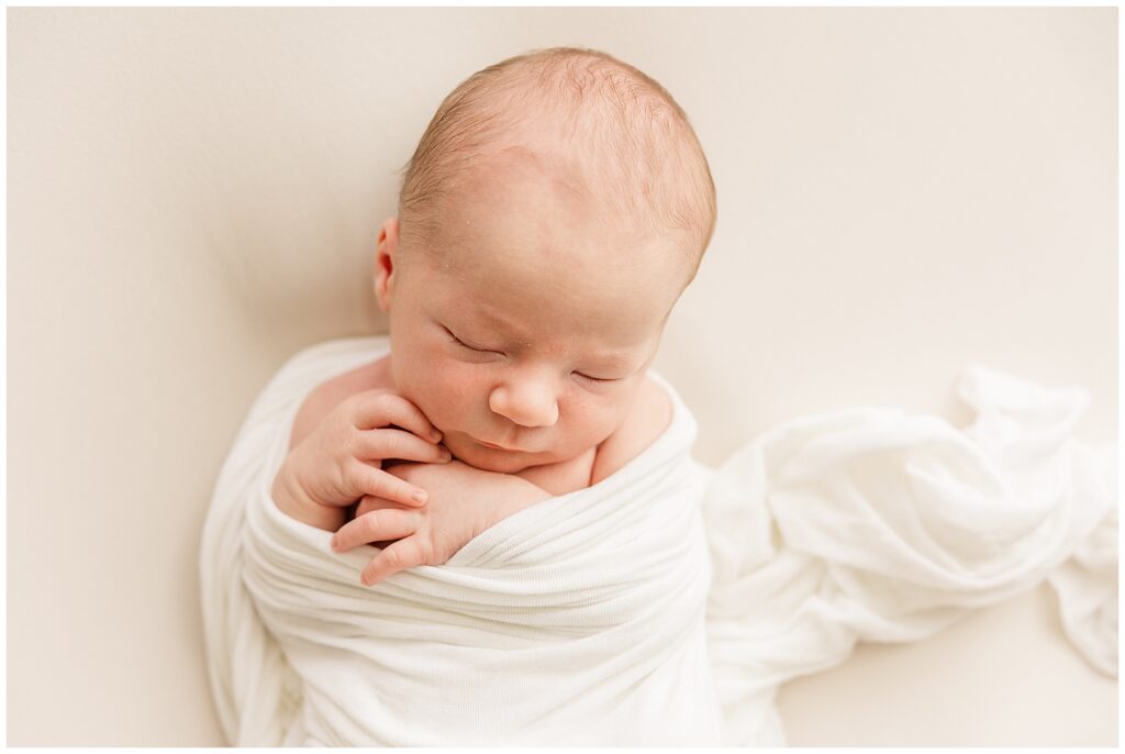baby sleeps with hands out of his swaddle during newborn photos 