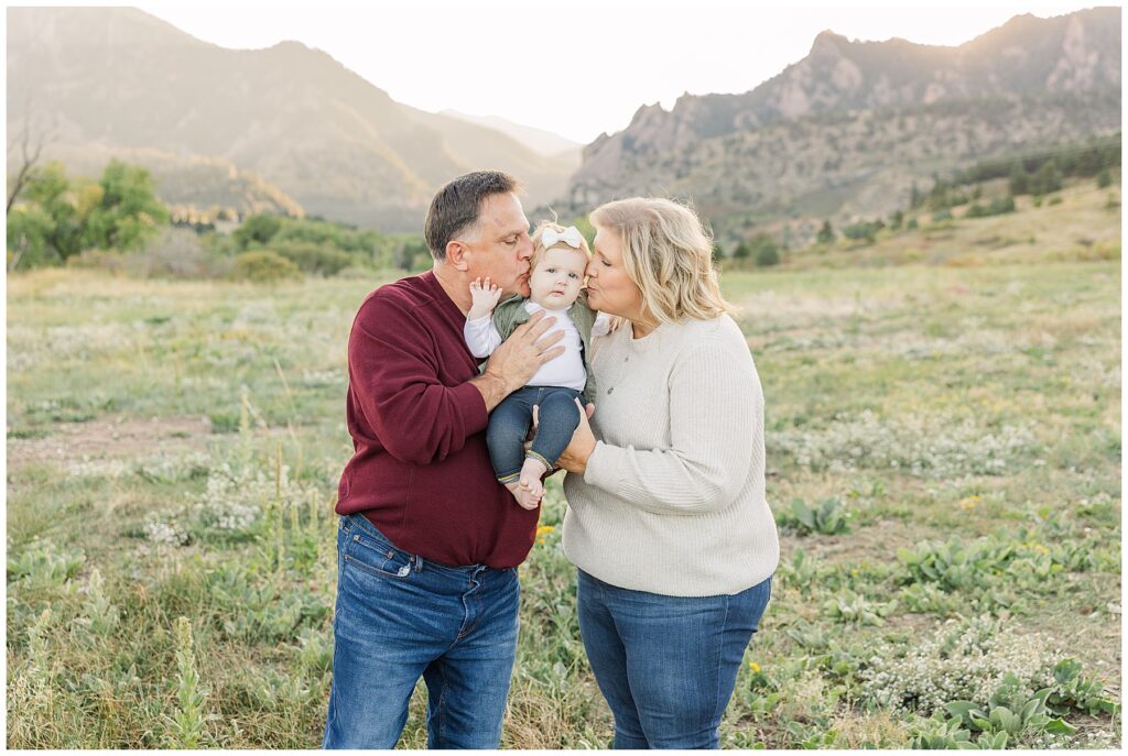 Baby is held by both grandma and grandpa as they kiss her on the cheeks during the Stute Family Outdoor Session at South Mesa Trailhead in Boulder, CO