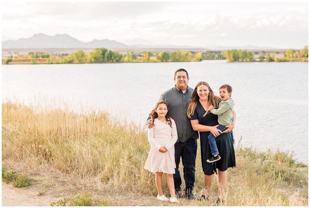 Family of four stand and pose in front of a lake for Romero Family Fall Session at Standley Lake in Westminster, CO