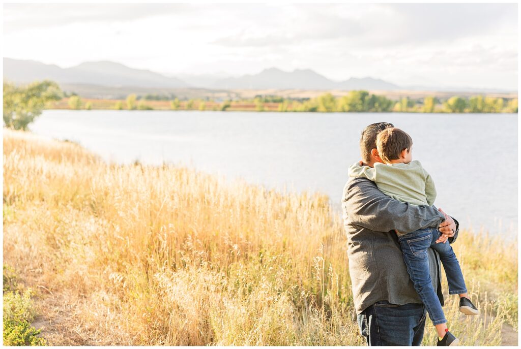 Father holds his toddler son and looks out over the a lake for light and airy photos with Catherine Chamberlain Photography