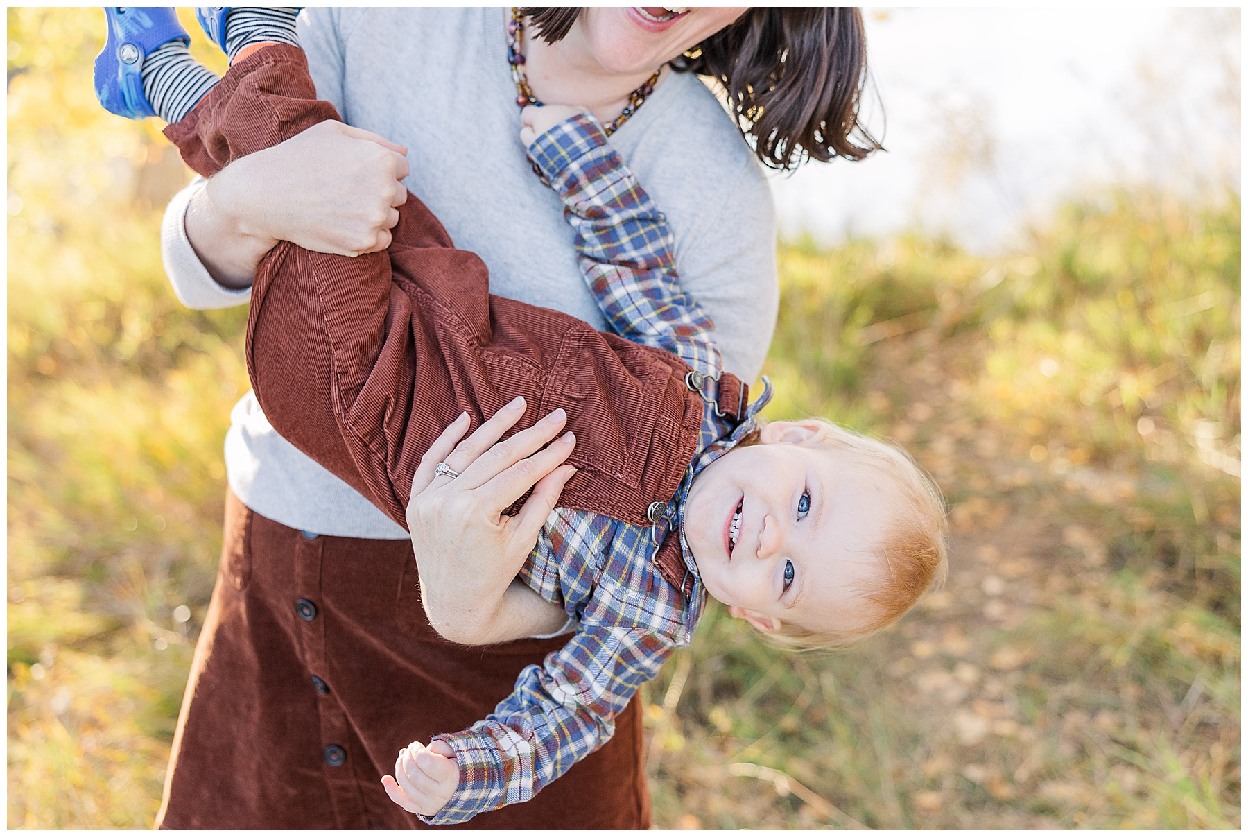 Mother holds her toddler boy upside-down for outdoor fall family photos with light and airy photographer Catherine Chamberlain