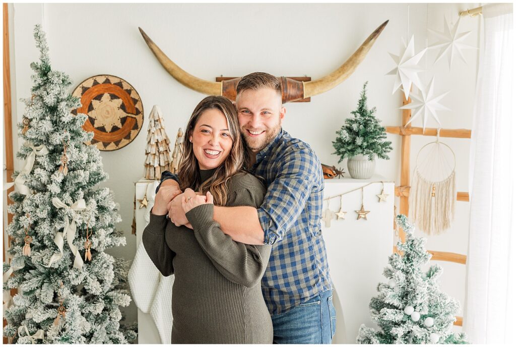 Husband wraps his arms around his wife as they pose for light and airy studio photos during Christmas mini sessions