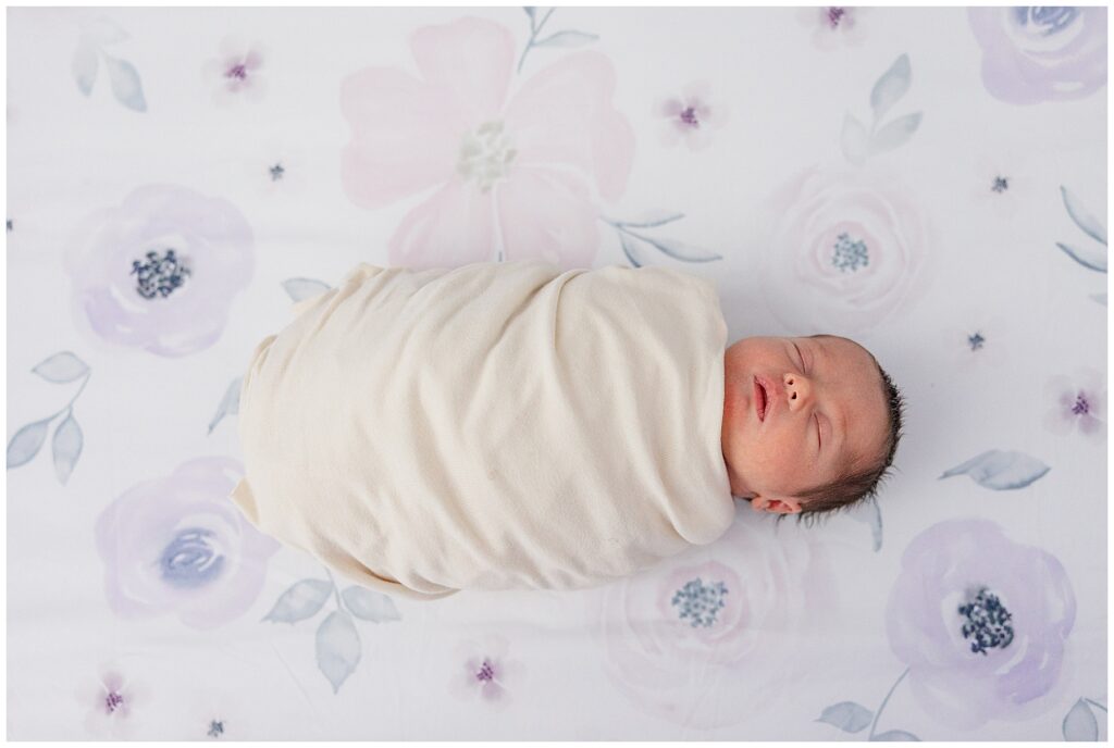 Precious newborn baby girl sleeps swaddled on her flower printed purple sheet