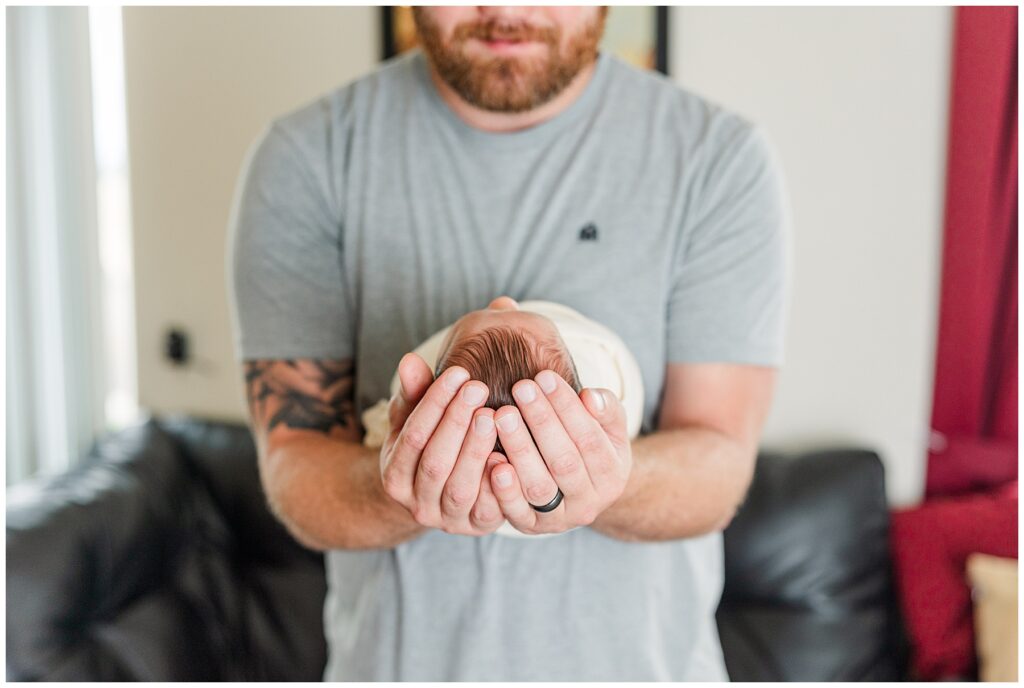 Dad holds precious newborn baby girl in his forearms during light and airy in-home newborn photos