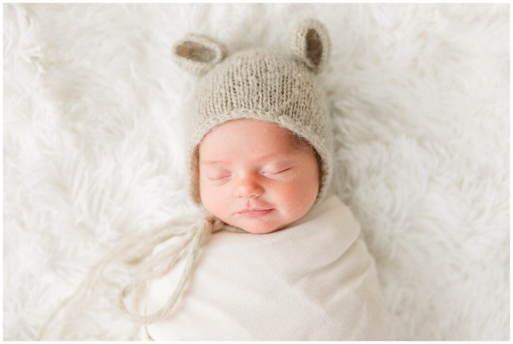 Precious newborn baby girl sleeps with smile on her face and hat with ears on her head