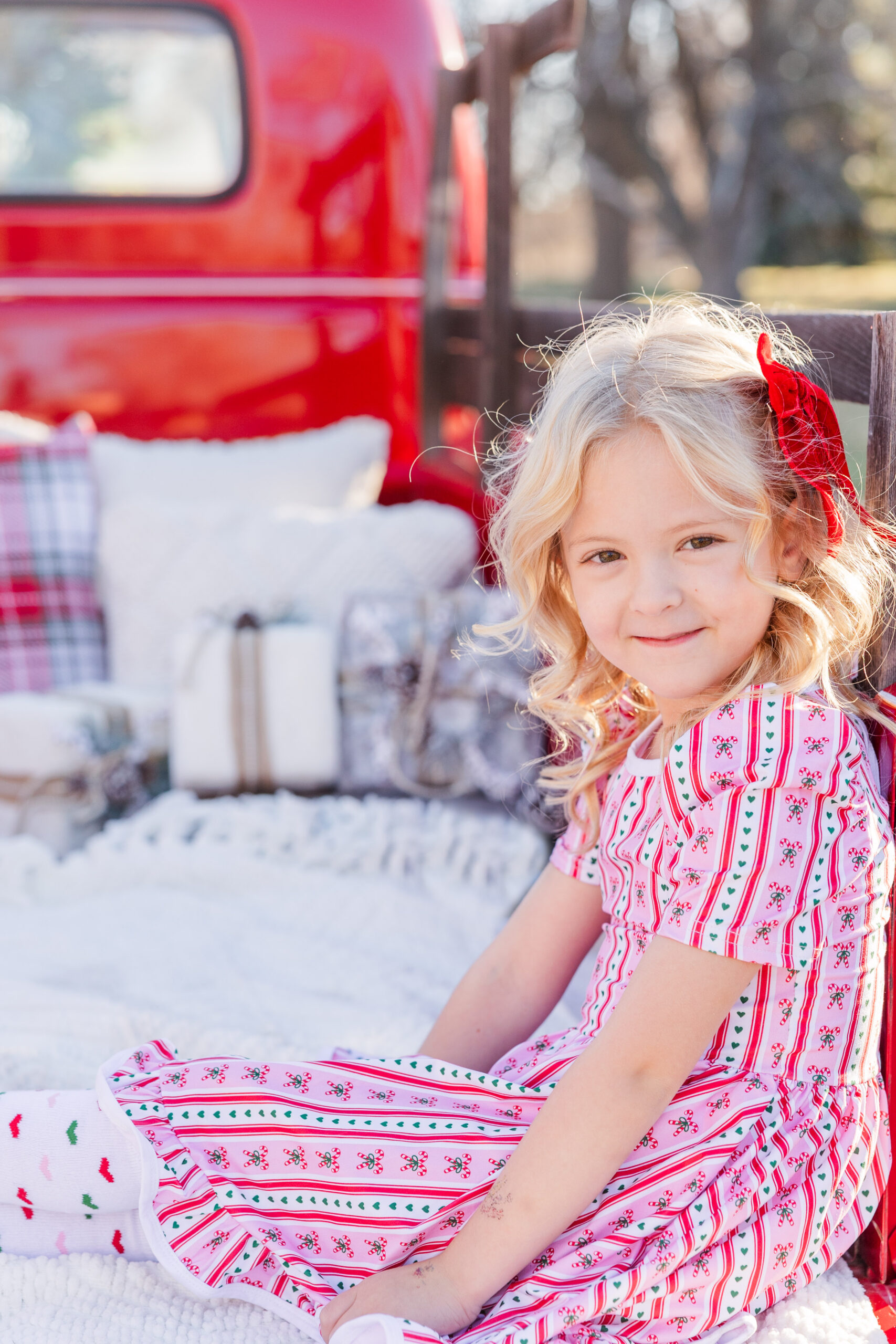 Little girls sits sideways in the back of an old bright red pick up truck for Christmas photos