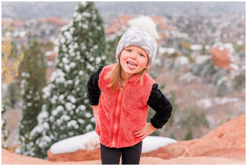 Little girl poses with her tongue out and hands on her hips during snowy outdoor family minis 