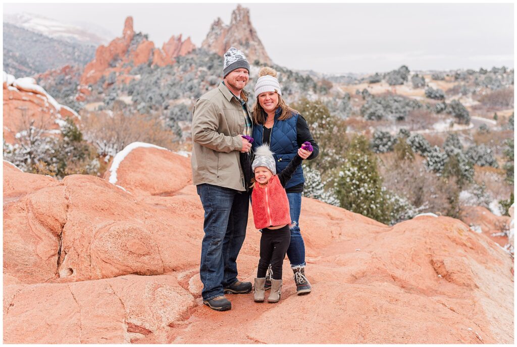 Family of three pose standing on a red rock formation for light and airy photos with Catherine Chamberlain Photography