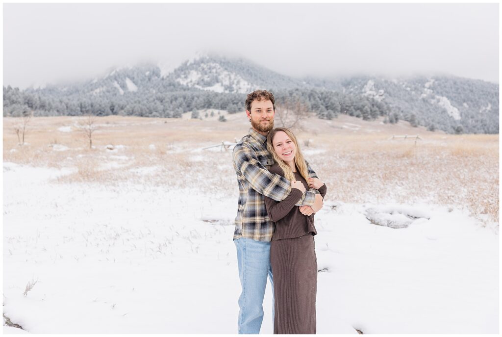 Couple pose facing the same direction but look to the camera for a light and airy snowy session