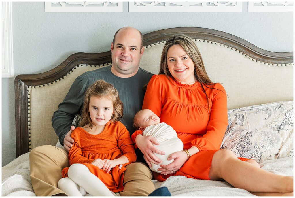 New family of four pose on their bed for newborn photos