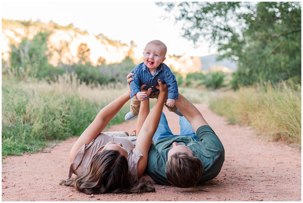 Parents lay on a path and hold up a baby facing the camera taken by Catherine Chamberlain Photography