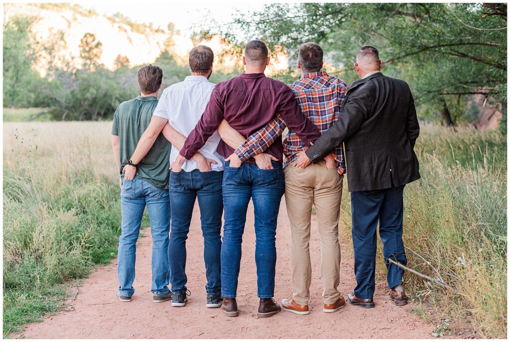 Men of the family do a silly pose with hands in the back of each other's pockets 