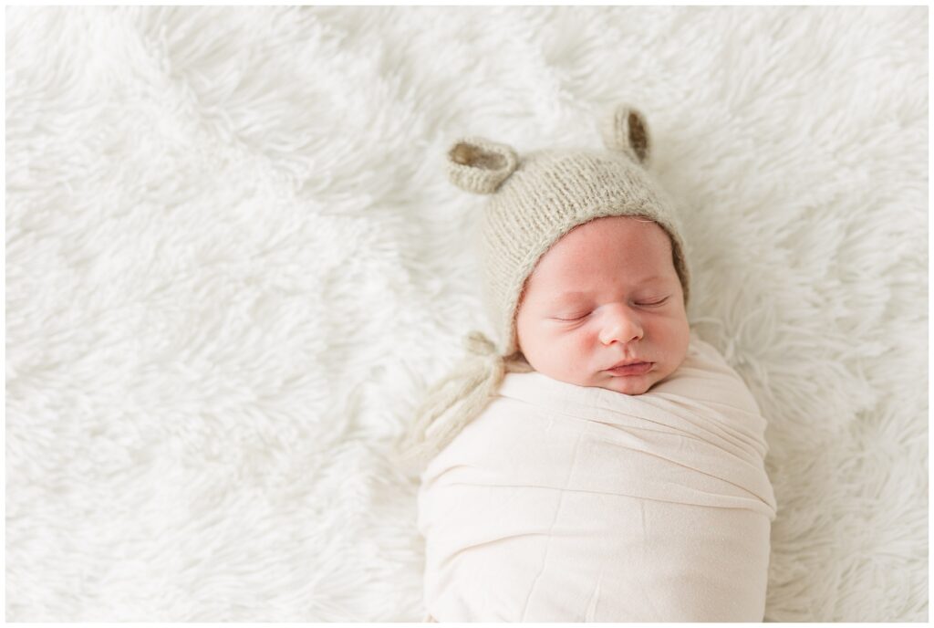 Newborn swaddled in white on a shag carpet in a hat with ears