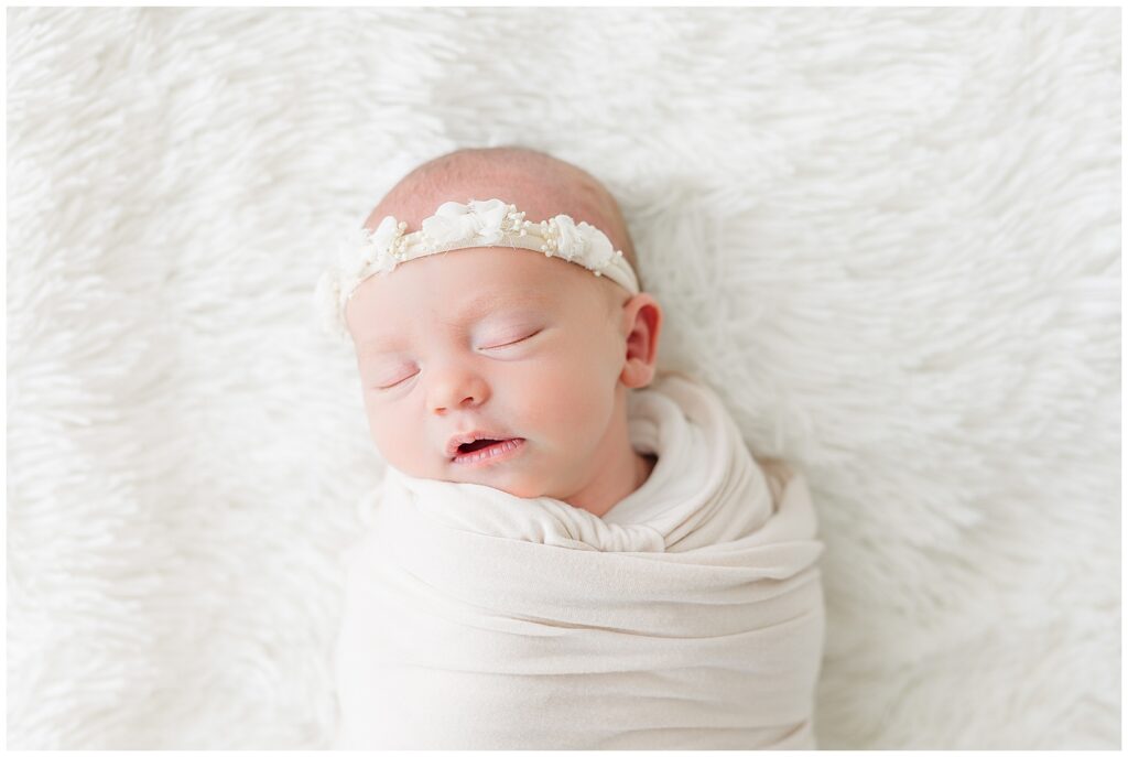 Baby girl swaddled in white sleeps with her headband on