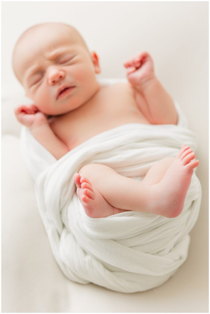 Light and airy picture of a newborn sleeping in a swaddle with her hands up during a Denver indoor newborn session with Catherine Chamberlain