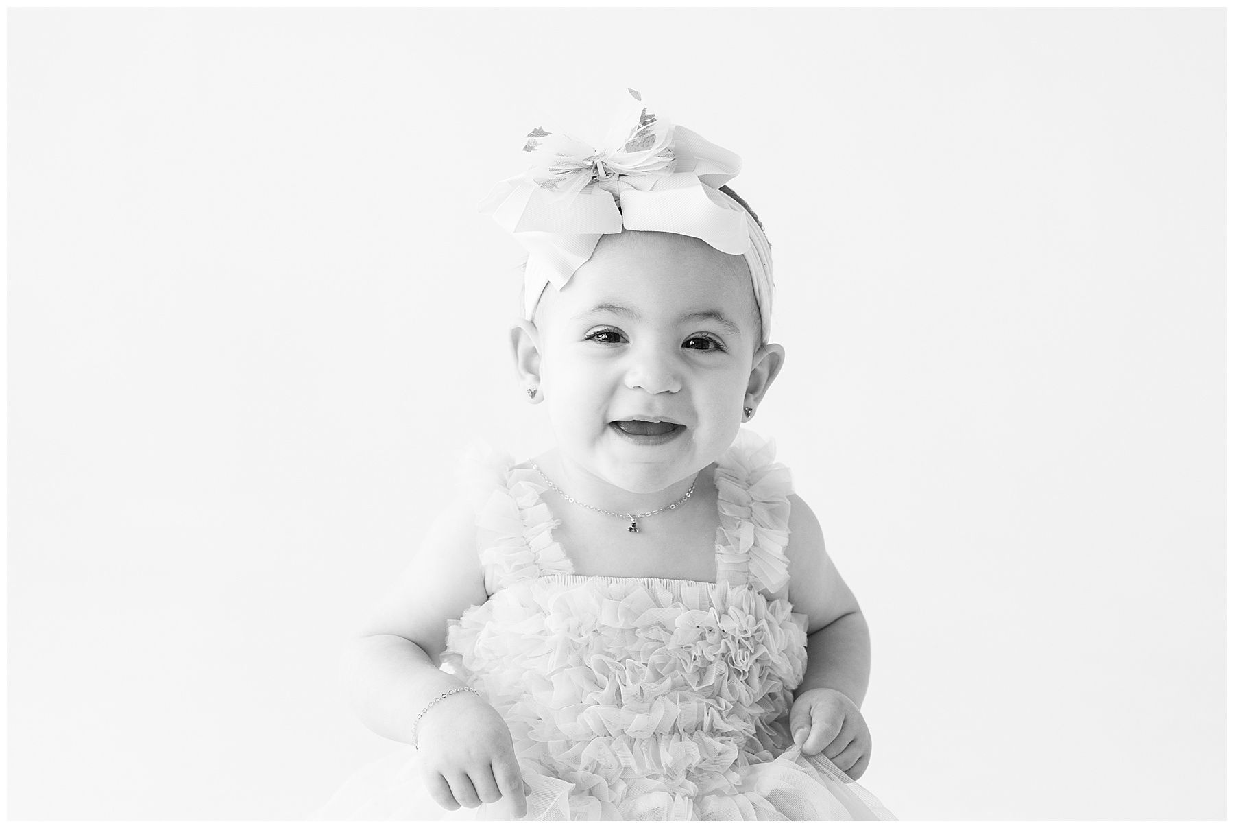 Baby girl in a ruffled dress and headband sit posing for Catherine Chamberlain during a light and airy session in Denver, CO