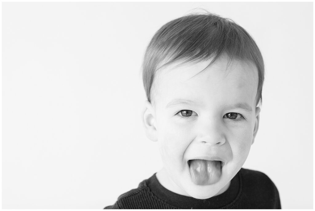 Close-up shot of a little boy wearing black sticking his tongue out at the camera