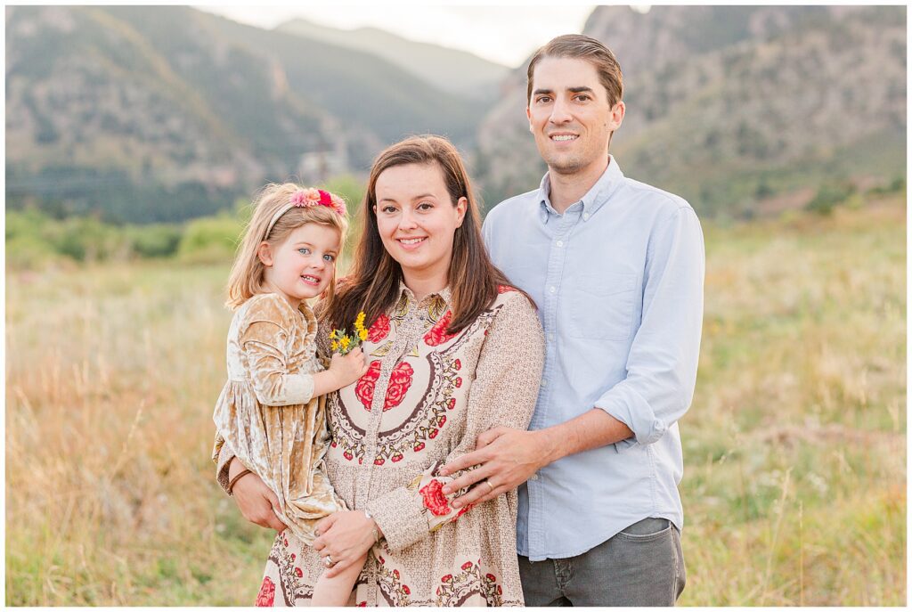 Family of three stand together and pose in front of Colorado mountains