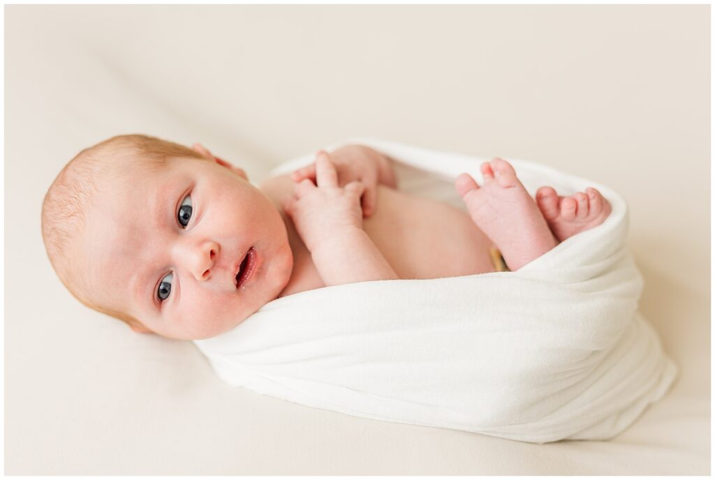 Baby is swaddled and looking away from the camera during light and airy photos with Catherine Chamberlain