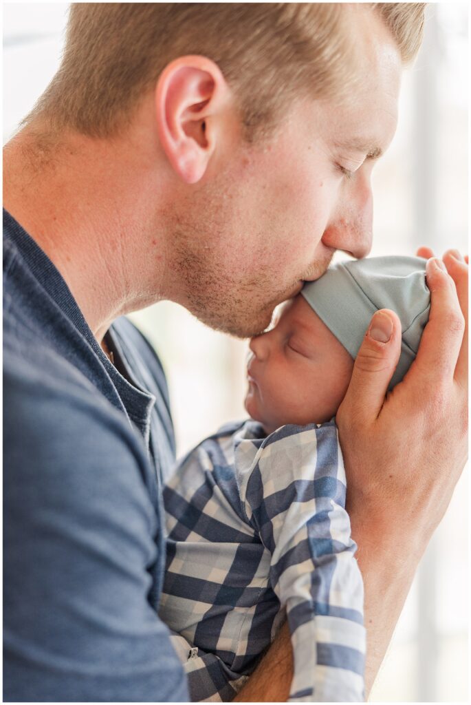 Dad kisses baby on the head in this educational blog about newborn session safety considerations