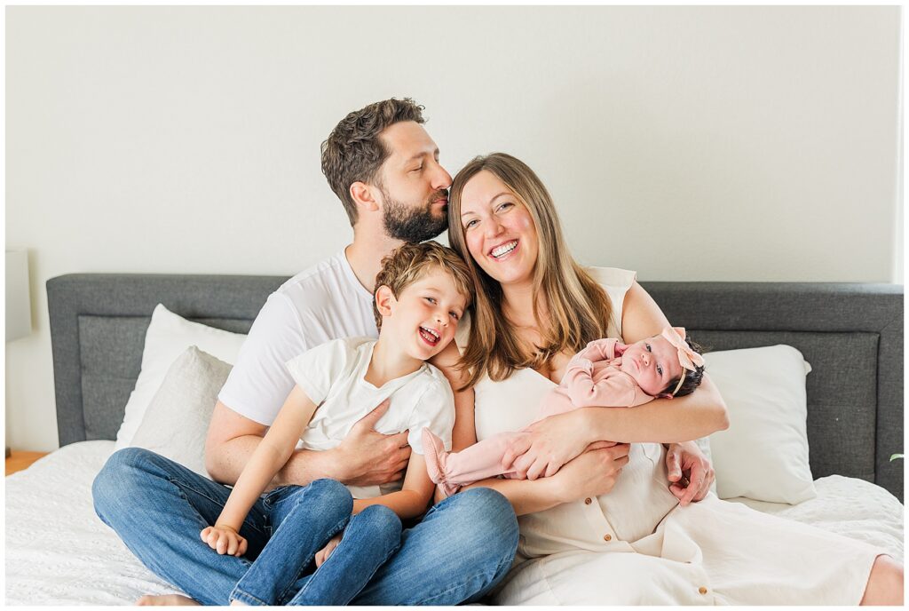 Family of four have a candid shot on the bed for a blog titled Newborn Photoshoot Wardrobe Guide