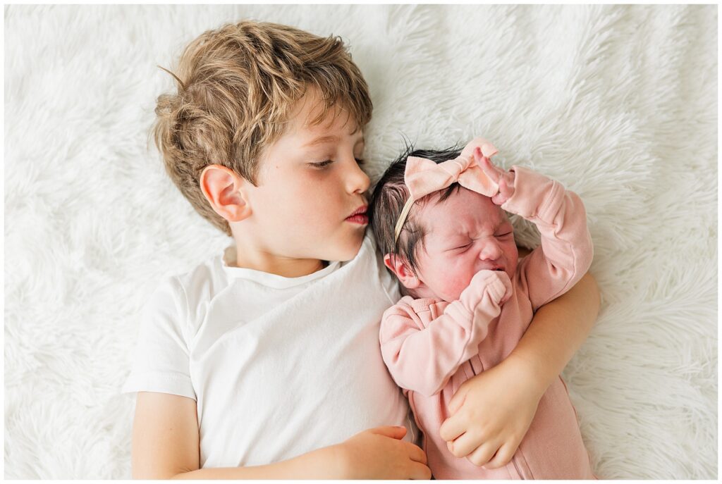 Little brother holds his newborn sister on the floor for lifestyle newborn photos
