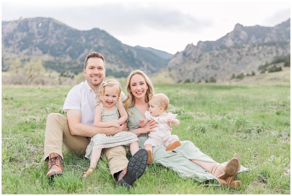 Family sits on the green grass with Boulder flatirons behind them