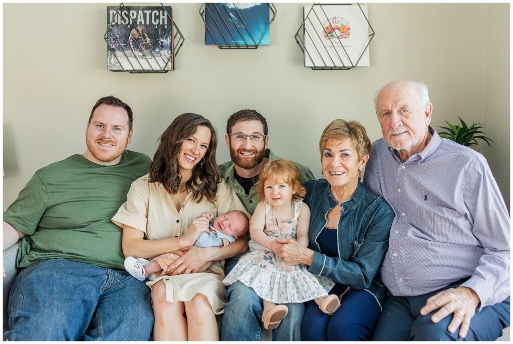 Extended family pose together on a couch for newborn photos featured in a blog discussing the importance of print
