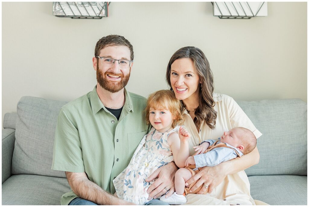 New family of four sit together for in-home lifestyle newborn photos