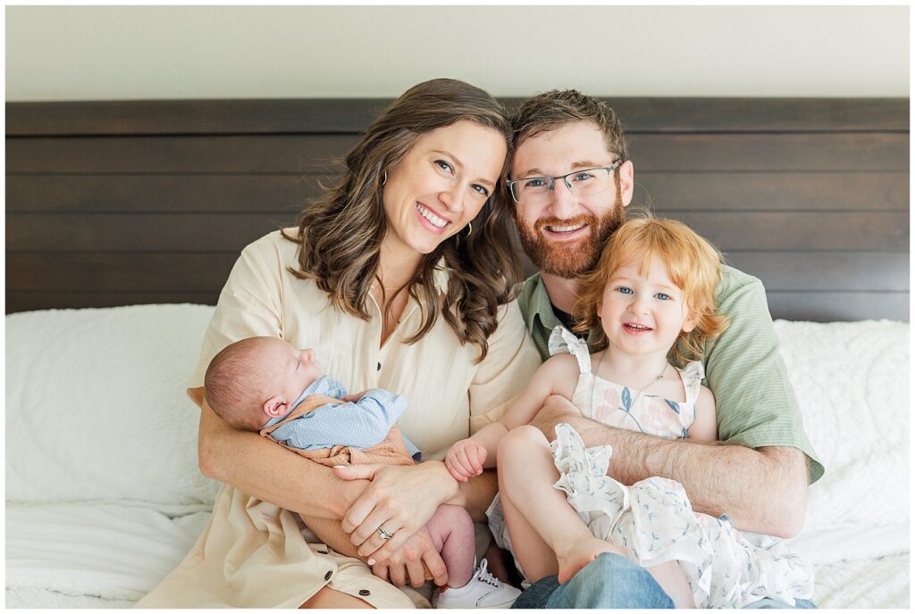 Family of four pose on their bed for newborn photos in their own home