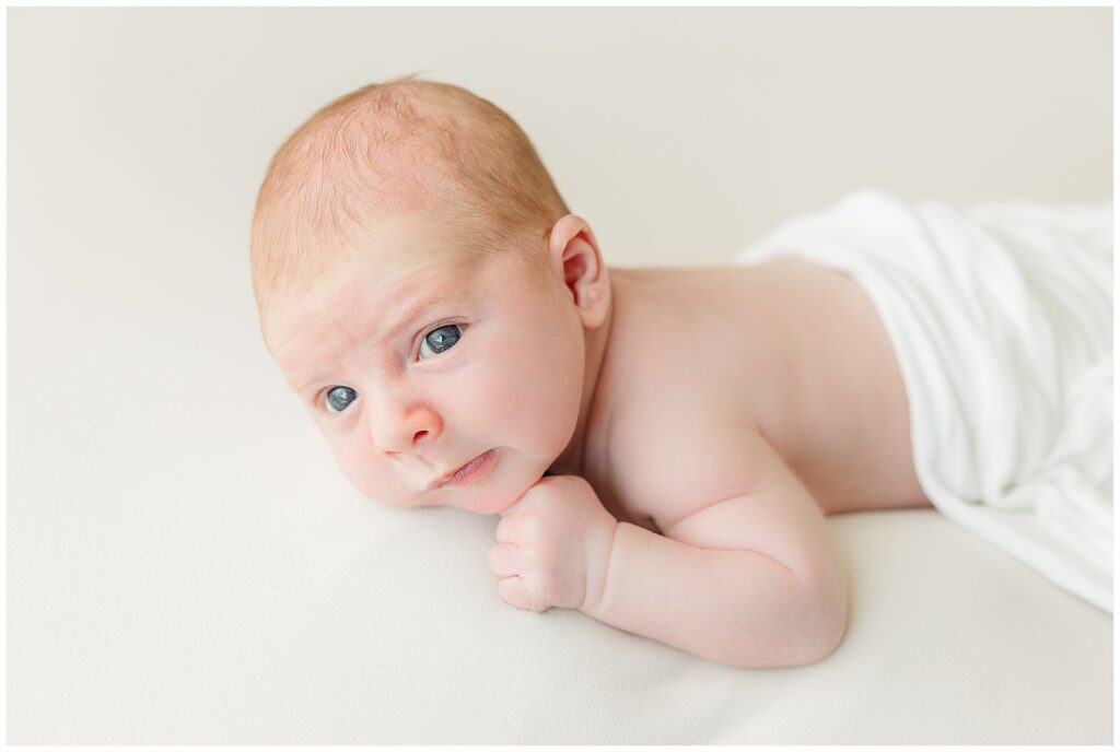 Newborn baby boy poses on his belly for light and airy photos
