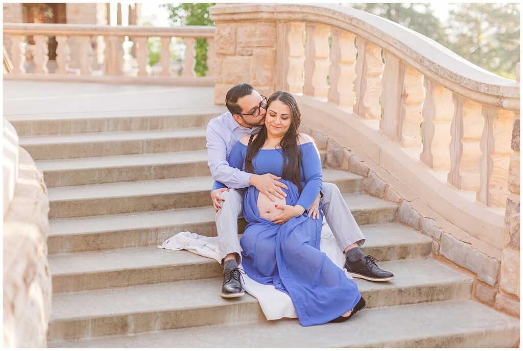 Expecting couple snuggle on a grand staircase during light and airy outdoor maternity photos