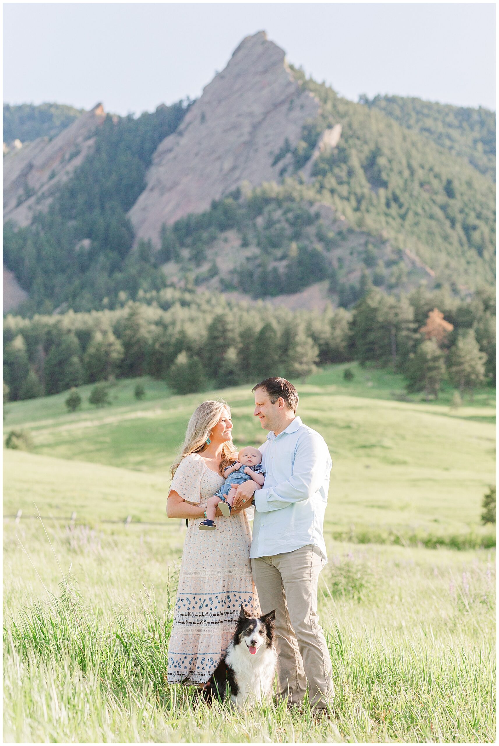 Couple looks at each other while holding their baby and posing with their dog at Chautauqua in Boulder, CO
