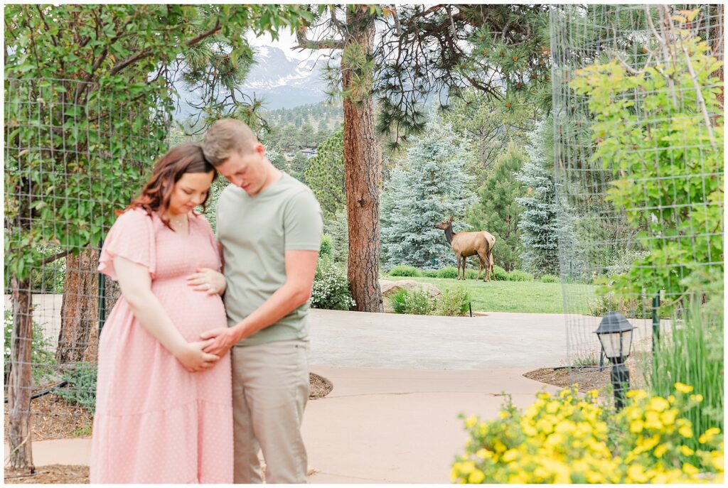 Expecting couple pose with their heads together while holding hands and looking at her belly