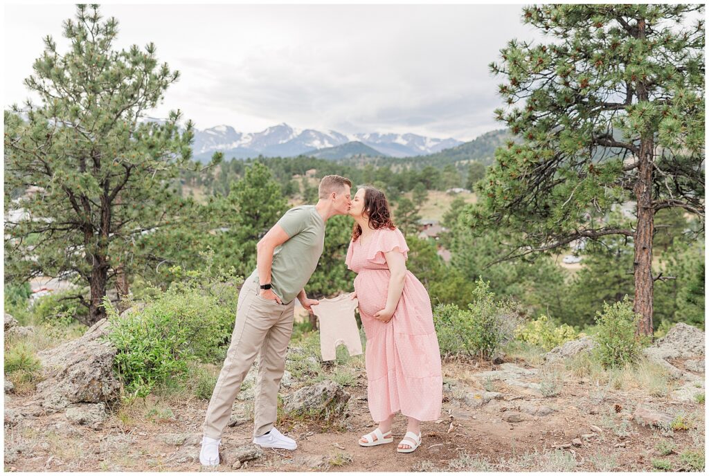 Couple share a kiss while holding a baby outfit 