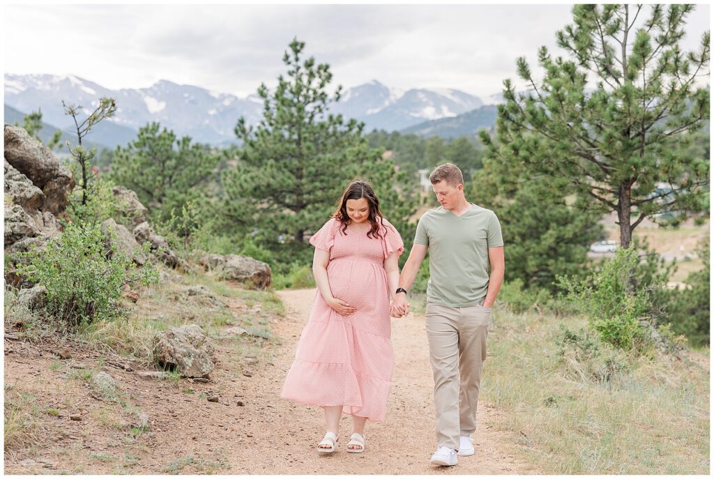 Couple walk hand-in-hand while she holds her belly and they look down at it