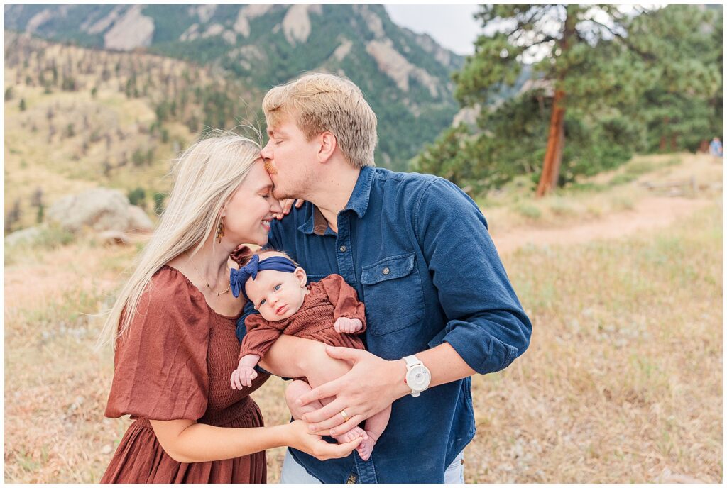 Mom and dad share a tender kiss while holding their baby girl during outdoor fall mini sessions with Catherine Chamberlain Photography