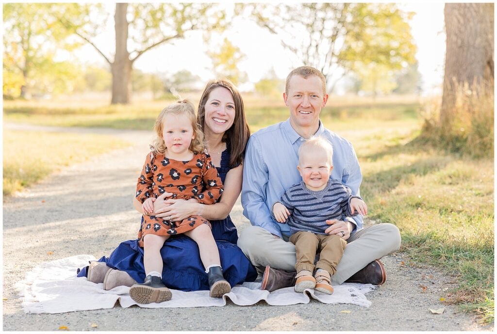 Family of four pose on the ground for fall minis and are featured in a blog on the Benefits of Morning Sessions for Families