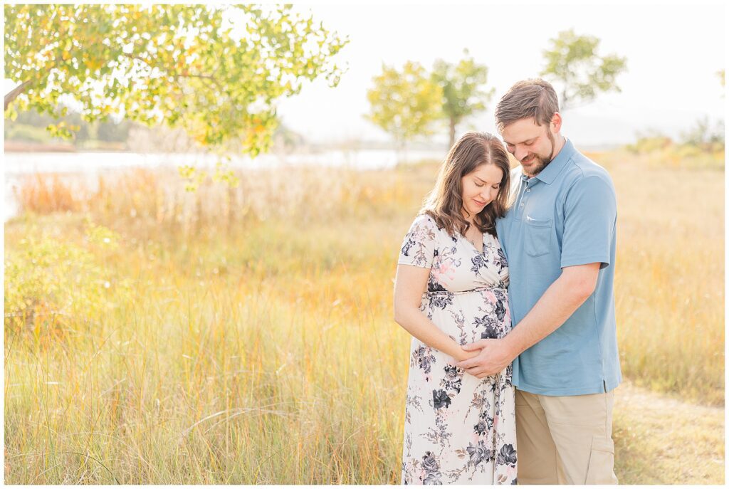 Expecting couple looks down at her belly while holding hands