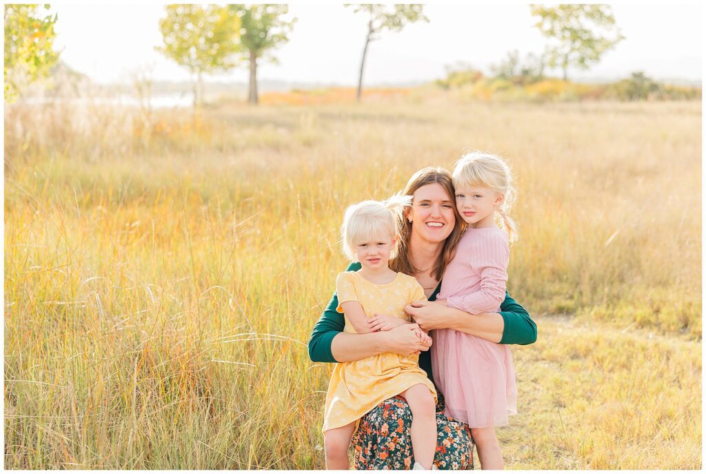 Mom squats down and holds her two daughters for fall minis at McIntosh Lake