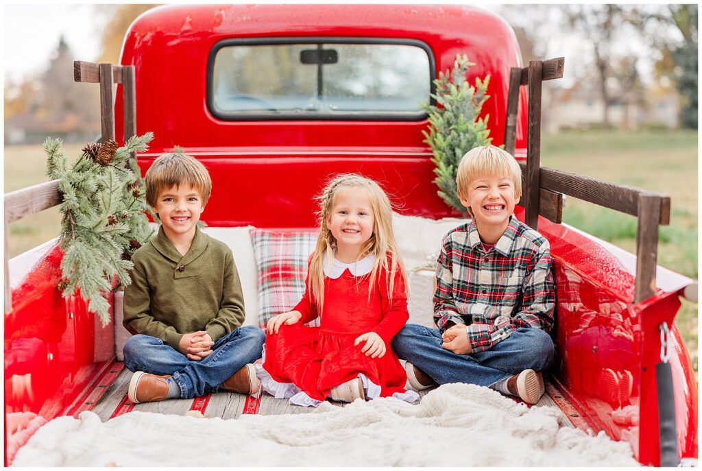 Siblings pose for Christmas minis outside in a bright red truck