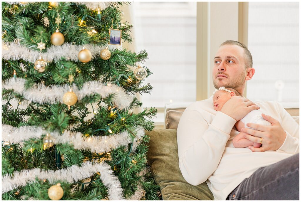 dad and baby girl pose by the Christmas tree for professional photos