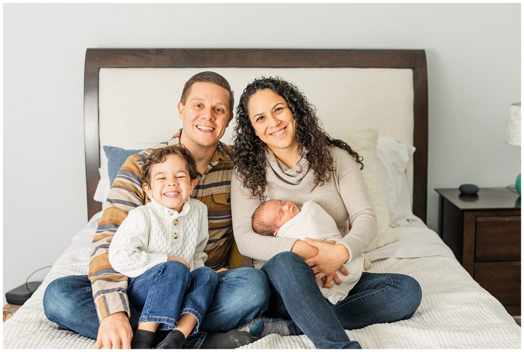 Family of four pose on their bed during in-home newborn photo session