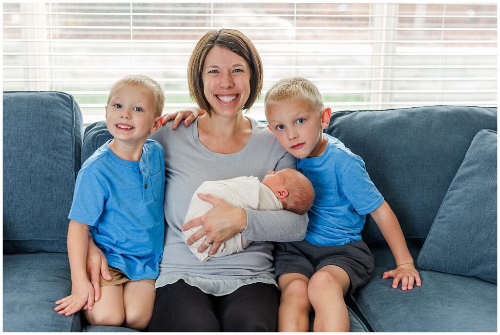 Mom smiles with her three sons during a newborn photoshoot session taken by Catherine Chamberlain
