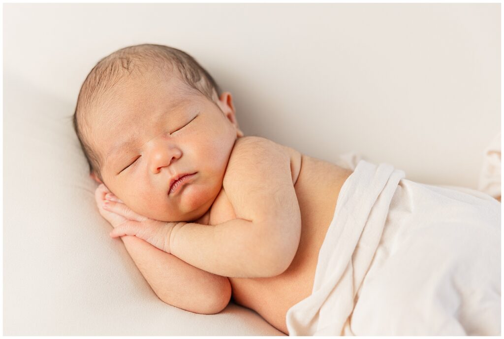 Newborn sleeps with hands under chin while swaddled